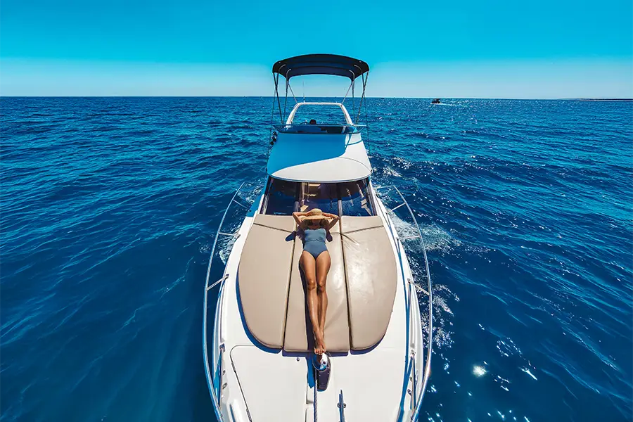 Woman relaxing at the front of a yacht on crystal-clear blue water under an open sky, during a Mediterranean-style boat tour