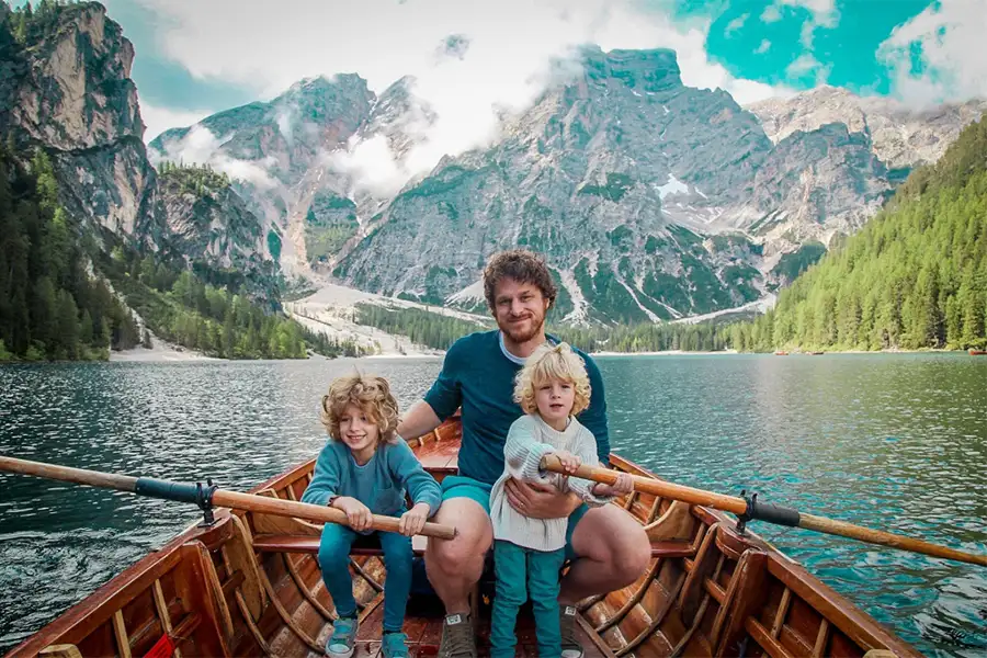 Father with two children on a boat ride on Lake Braies, surrounded by the Dolomite mountains, during a family trip to Italy.