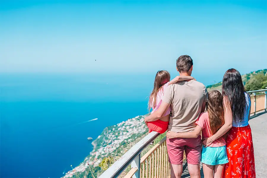 Family enjoying the stunning view of the Amalfi Coast during a family trip to Italy, on a sunny day with the blue sea in the background.