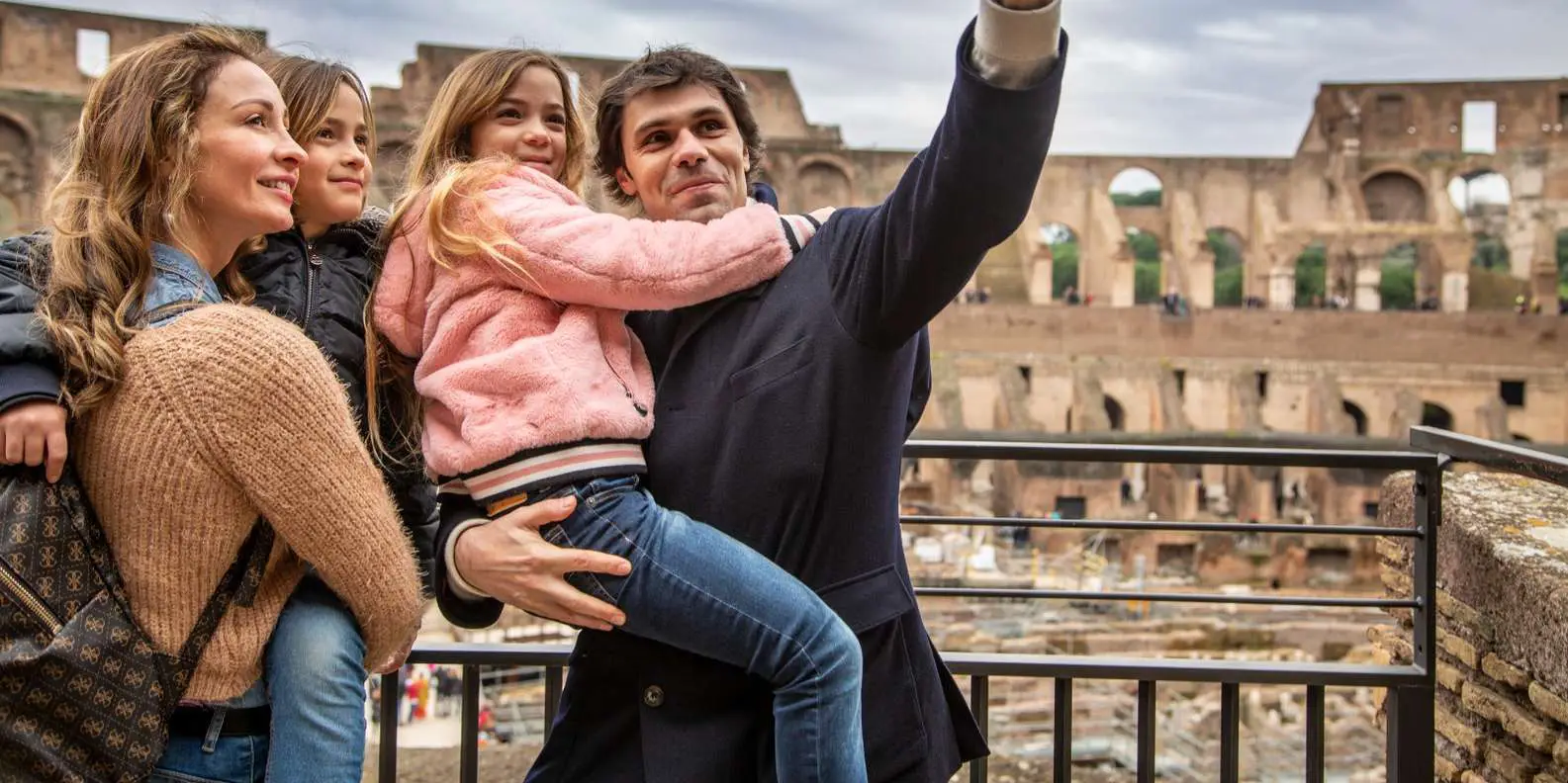 Smiling family posing at the Colosseum in Rome during a family trip to Italy, on a sunny day.