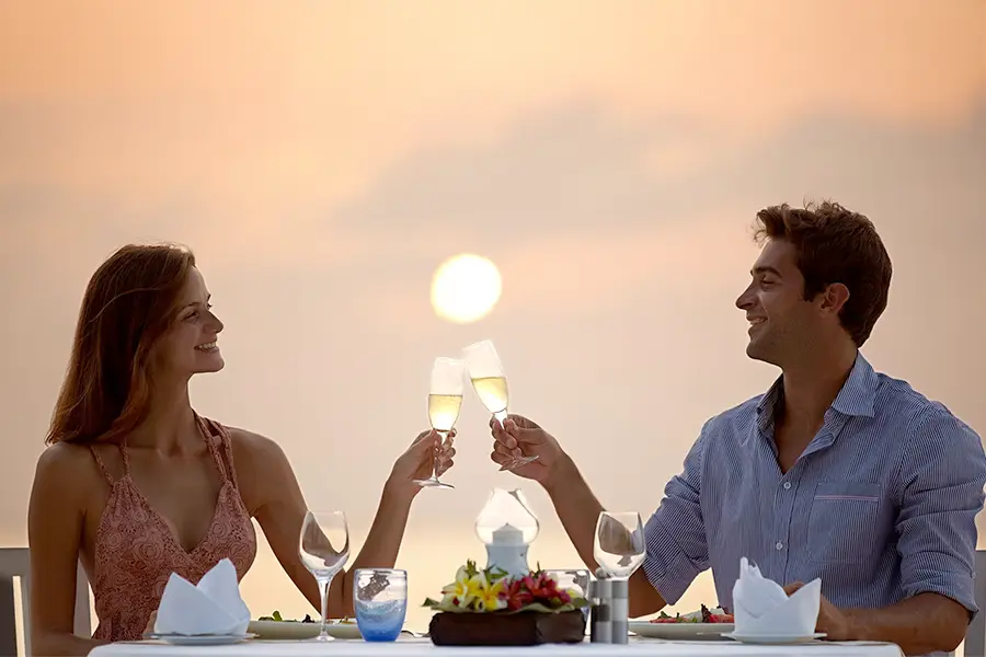 Couple toasting at sunset during a romantic outdoor dinner, with glasses of sparkling wine and an intimate atmosphere.