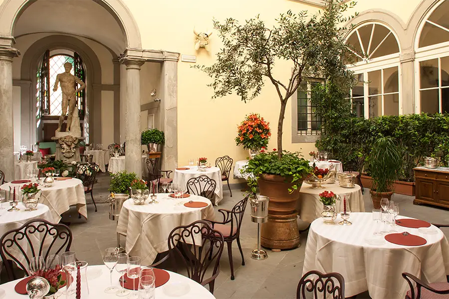 Elegant courtyard of Enoteca Pinchiorri in Florence, with outdoor tables, greenery, a Renaissance statue, and a refined atmosphere.
