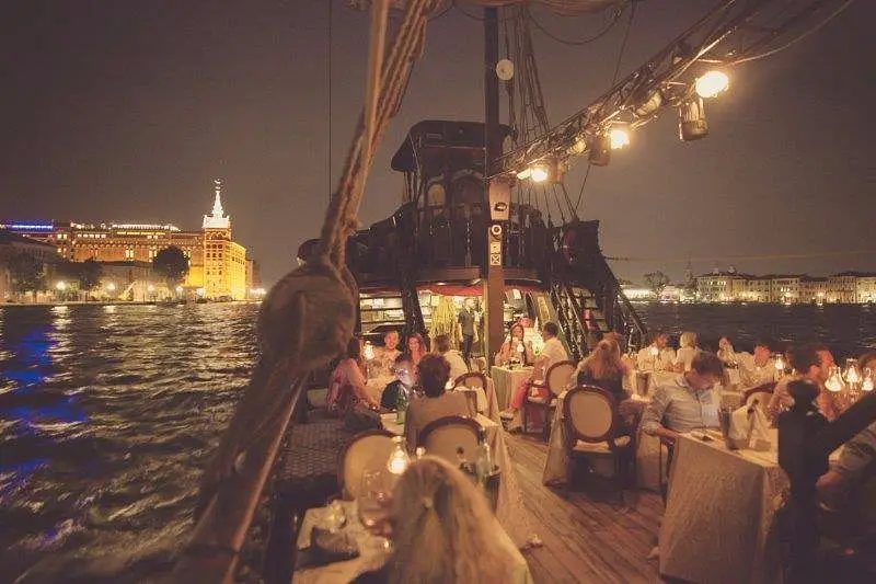 Candlelight dinner aboard the Galeone Veneziano in Venice, with a nighttime view of the city reflected in the waters of the lagoon.