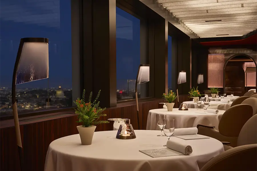 Elegant setting of La Pergola restaurant in Rome, with finely set tables and a panoramic night view of the Eternal City.
