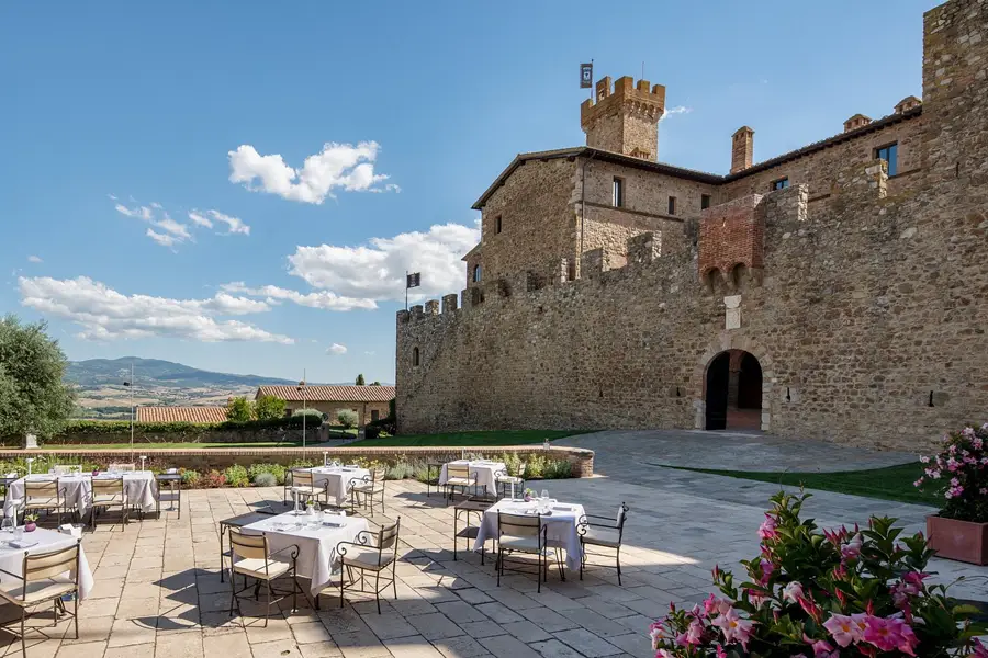Outdoor tables in the stone courtyard of La Sala dei Grappoli restaurant in Montalcino, with a view of vineyards and a medieval castle