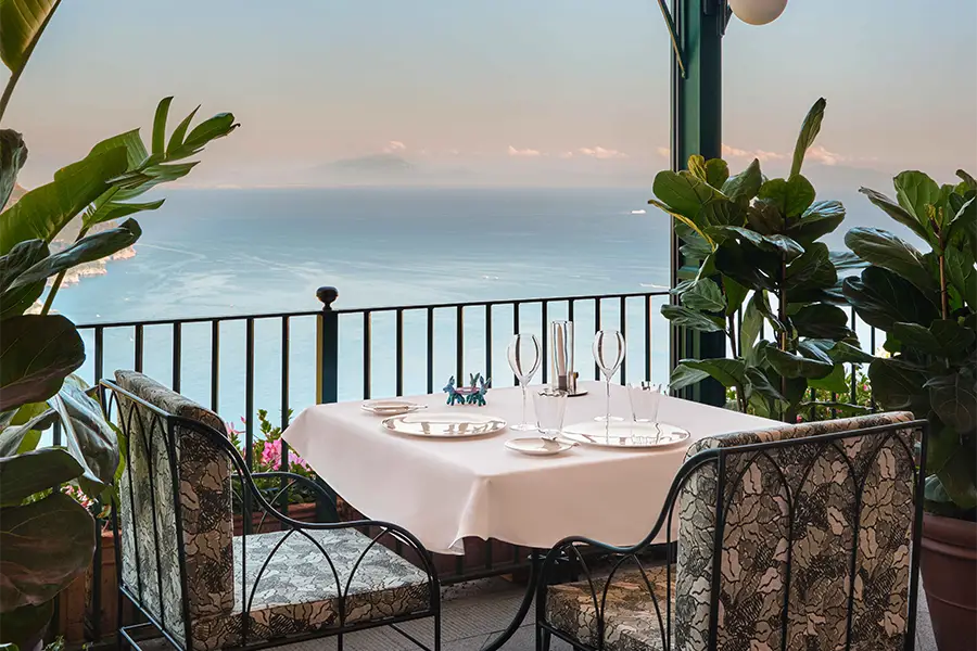 Elegantly set outdoor table with a view of the Mediterranean Sea, surrounded by plants on the terrace of Palazzo Avino restaurant on the Amalfi Coast