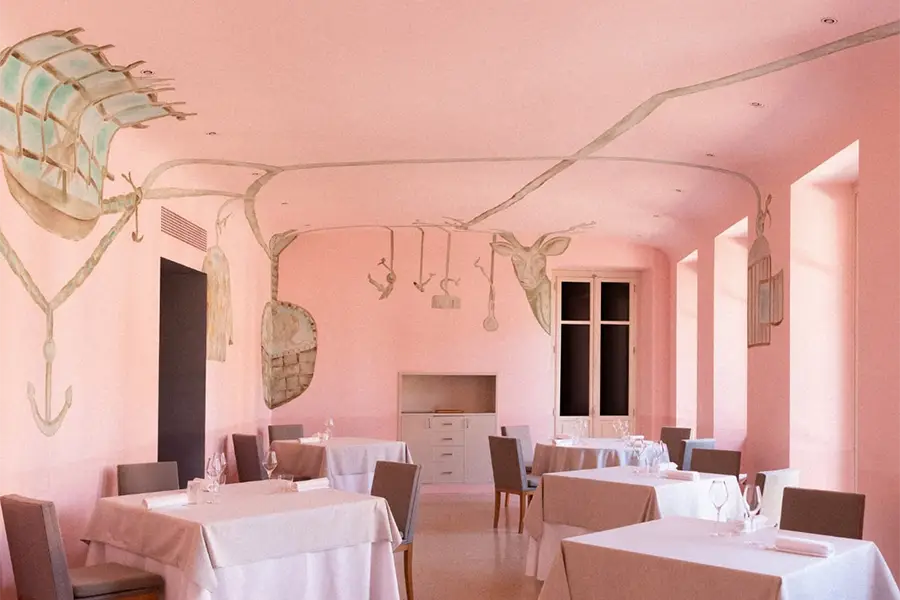 Dining room with artistic pink-toned decor, elegantly set tables, and natural lighting at Piazza Duomo restaurant in Alba