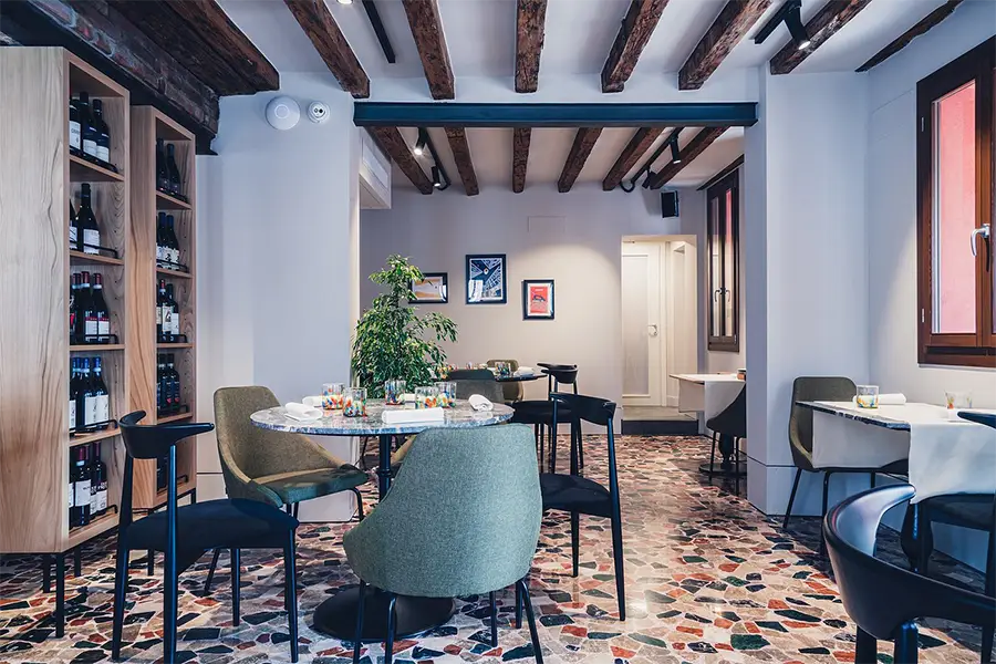 Cozy dining room at Wisteria restaurant in Venice, with colorful stone flooring, wooden beam ceiling, and elegant tables